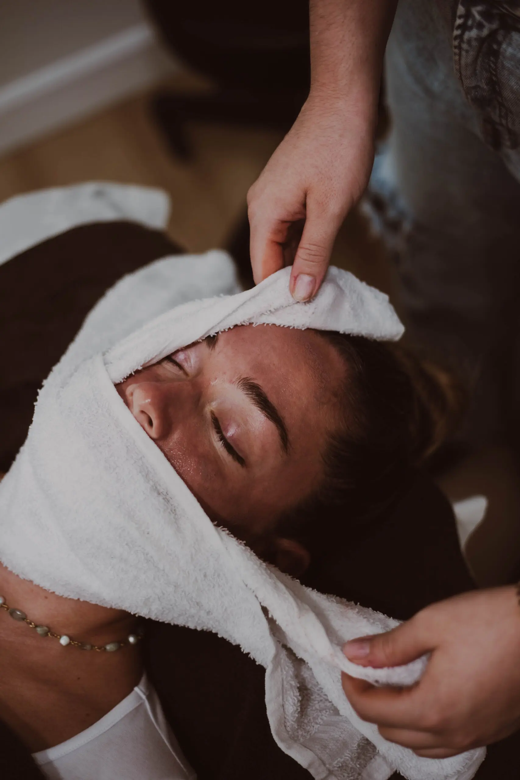 Client receiving a facial treatment, wrapped in a warm towel